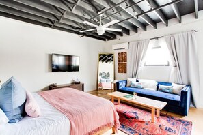 Ein modernes Schlafzimmer mit einem Bett, einer Couch, einem Fernseher und einem Fenster mit Vorhängen.