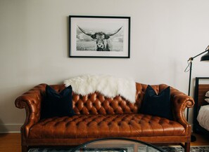 Un canapé en cuir marron agrémenté d’un plaid en fausse fourrure blanche, de deux coussins foncés et d’un tableau représentant un taureau, accroché au mur.
