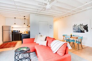 Ein modernes Wohnzimmer mit einem roten Sofa, einem kleinen runden Tisch und einem Essbereich mit blauen Stühlen.