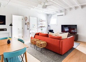 Ein modernes Wohnzimmer mit einem roten Sofa, einem Esstisch mit Stühlen, einem Fernseher und einem Deckenventilator.