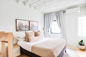 A bedroom with a bed, bedside tables, a window with curtains, and wall art. - Market #8 · Stellar Suites | The  Sunset Suite | NuLu | Bikes (Louisville)