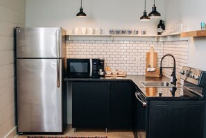 A compact kitchen with a stainless steel refrigerator, a microwave, and a sink. - Market #8 · Stellar Suites | The  Sunset Suite | NuLu | Bikes (Louisville)