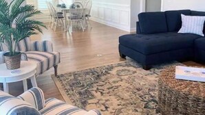 A living room with striped armchairs, a black sofa, a patterned rug, and a dining area in the background. - Carolina Skies Holden Beach ~3 min walk to beach. Guest Favorite! (Holden Beach)