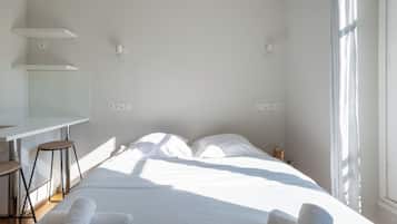 Ein schlicht eingerichtetes Hotelzimmer mit Bett, zwei Nachttischen, einem Schreibtisch und einem Fenster.