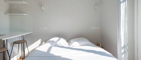 Habitación de hotel minimalista con una cama, dos mesitas de noche, un escritorio y un ventanal.