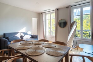Una sala de estar moderna con un sofá, una mesa de comedor con individuales y ventanas amplias con cortinas.