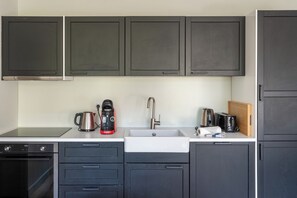 Una cocina moderna con armarios oscuros, un lavamanos de acero inoxidable y una cafetera.