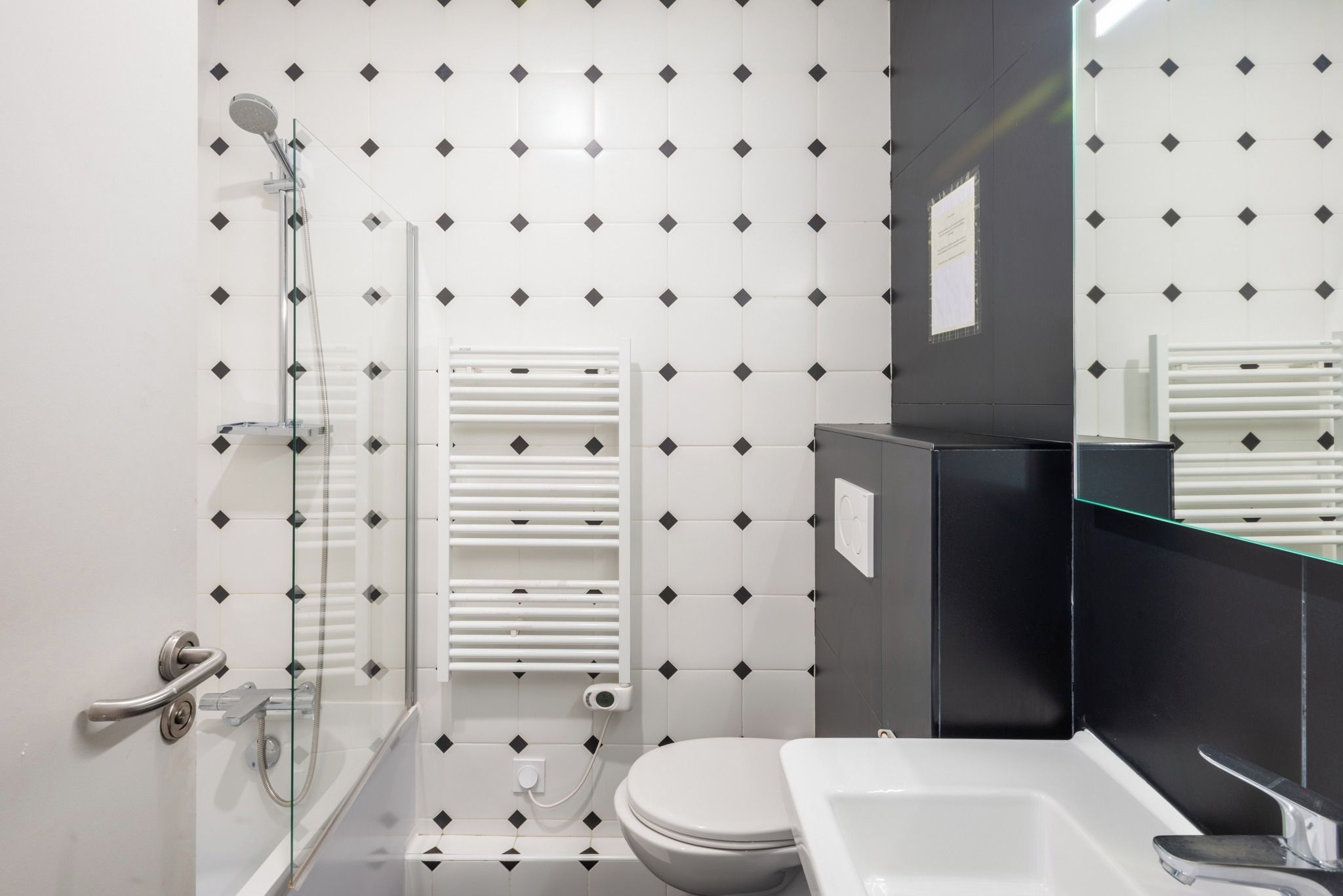 Une salle de bain moderne avec une douche à parois de verre, des toilettes blanches et un lavabo noir.