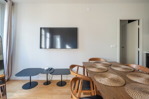 A modern dining area with a wooden table, woven placemats, and a flat-screen TV mounted on the wall.
