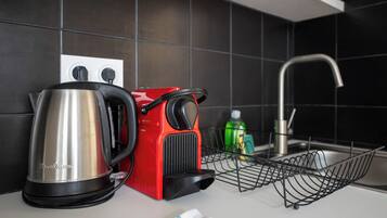 Een keuken met een waterkoker, een rode koffiemachine, een groene fles en een metalen rek.