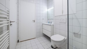 Et moderne badeværelse med toilet, håndvask og en brusekabine i glas.