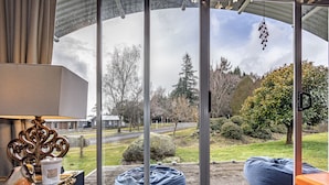 A room with a large glass door leading to a deck, a wooden bench, and a decorative metal piece. - Alpine Way Cottage - Ohakune Holiday Home (Ohakune)