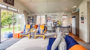A spacious living area with a blue sofa, two armchairs, a coffee table, and a kitchen area with a refrigerator and a sink. - Alpine Way Cottage - Ohakune Holiday Home (Ohakune)