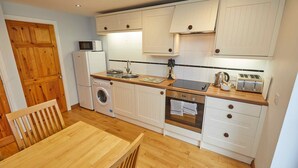 A compact kitchen with wooden cabinets, a washing machine, a microwave, a toaster, and a sink.