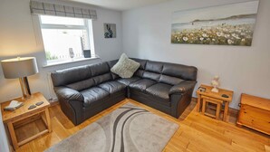 A modern living room with a leather sectional sofa, a wooden coffee table, a small side table, a lamp, and a painting on the wall.