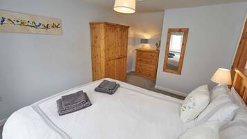 A neatly made bed with folded towels, a wooden wardrobe, a dresser, a mirror, and a wall-mounted artwork of birds.