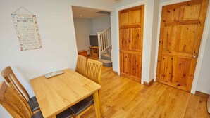 A dining area with a wooden table and chairs, a wall-mounted sign with rules for a better life, and wooden doors.