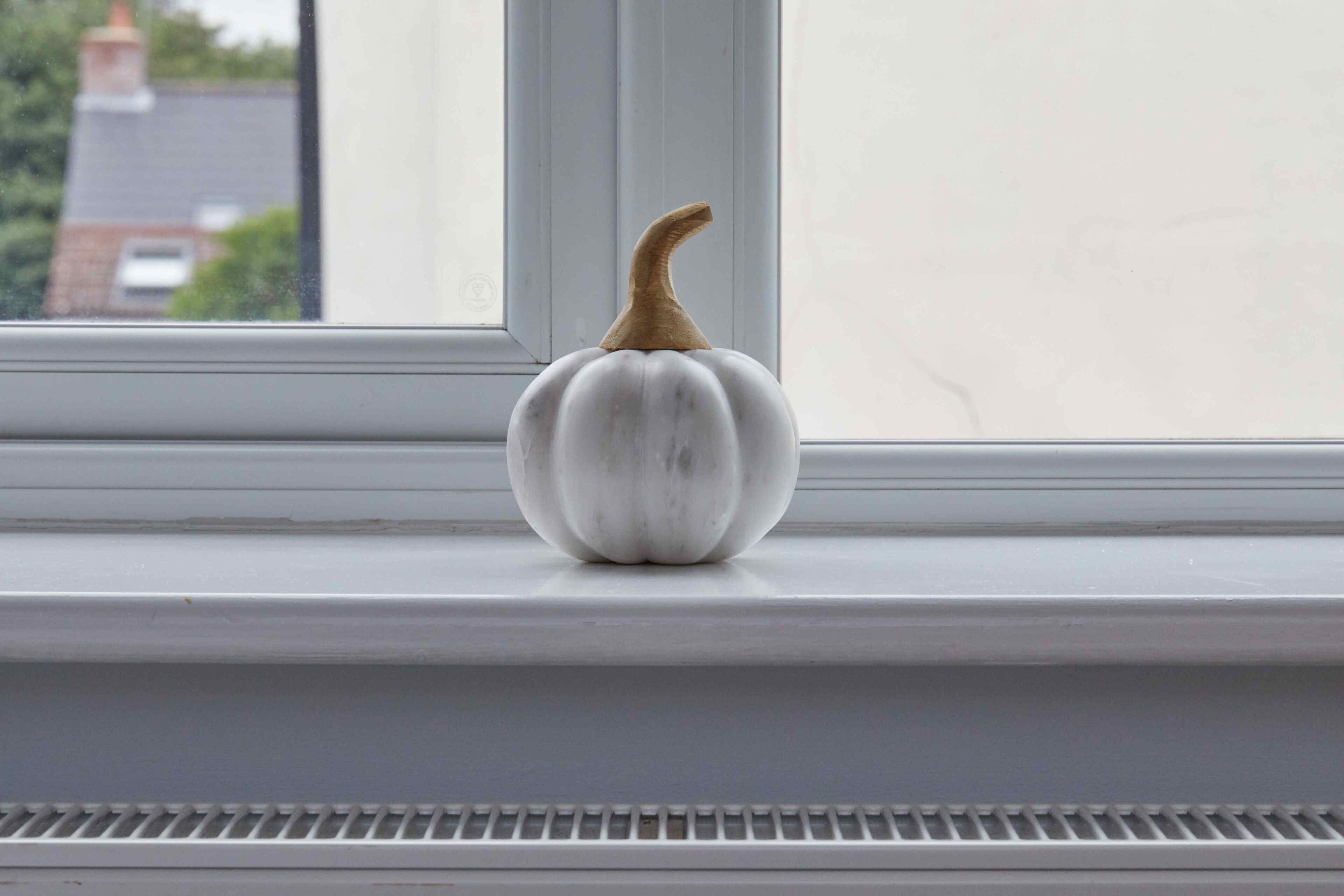 A white ceramic pumpkin on a window sill.