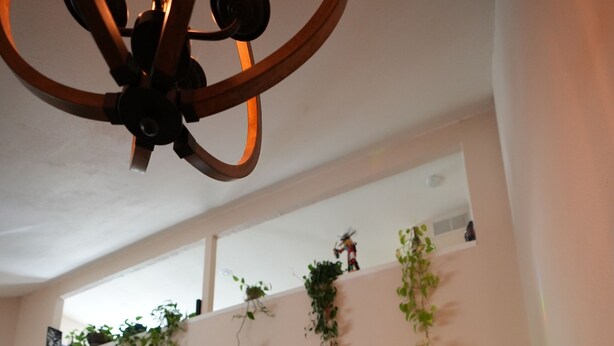 Un vaste espace de vie agrémenté d’un ventilateur de plafond en bois, d’un téléviseur à écran plat et d’une console de couleur verte.