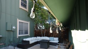 Un espace extérieur aménagé avec un salon de jardin, comprenant un canapé blanc, une petite table et des luminaires suspendus.