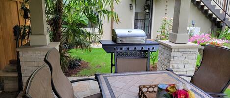 An outdoor patio with a grill, seating, and a view of a house.