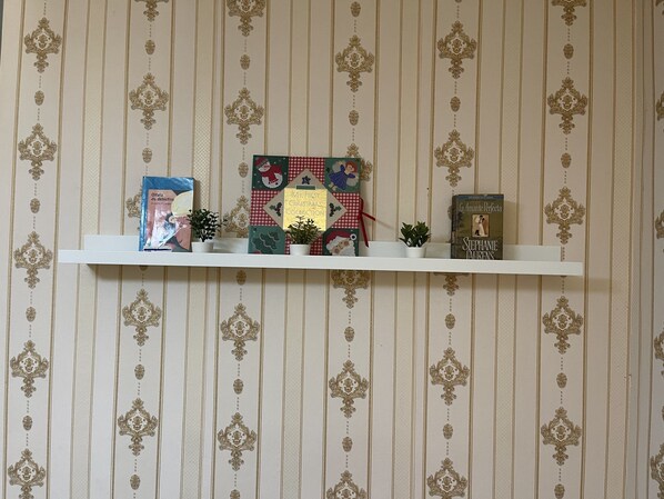 Une étagère avec des livres et de petites plantes en pot, le tout placé devant un mur recouvert de papier peint.