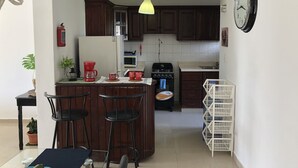 Una cocina con armarios de madera oscura, un refrigerador blanco, una estufa y un microondas. Hay un reloj en la pared y un extintor montado allí.