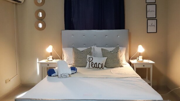 Una cama bien hecha con una almohada que dice 'Peace', dos lámparas de noche y una pared con tres espejos circulares y tres citas inspiradoras enmarcadas.