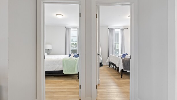Un pasillo de hotel con dos habitaciones, cada una con una cama, mesita de noche y ventana.