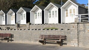 Eine Reihe weißer Strandhütten mit Fenstern, eine Steinmauer und Holzbanken.