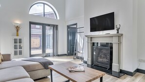 Ein geräumiges Wohnzimmer mit Kamin, einem darüber montierten Fernseher und einem großen Fenster, das für natürliches Licht sorgt.