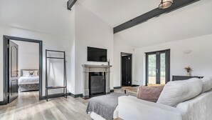 Ein geräumiges Wohnzimmer mit Kamin, einer Couch, einem an der Wand befestigten Fernseher und einer Tür zu einem weiteren Raum.