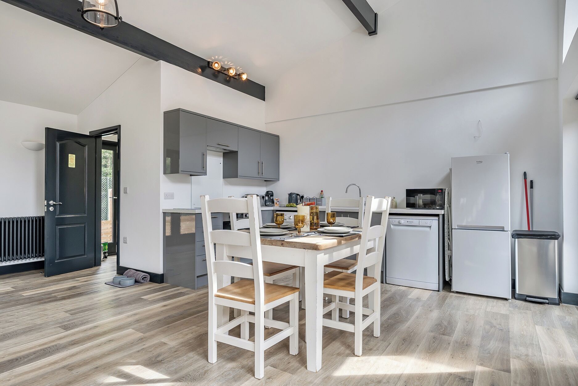 Una cocina moderna con una mesa de comedor preparada para cuatro personas, un microondas, un refrigerador y un lavamanos.