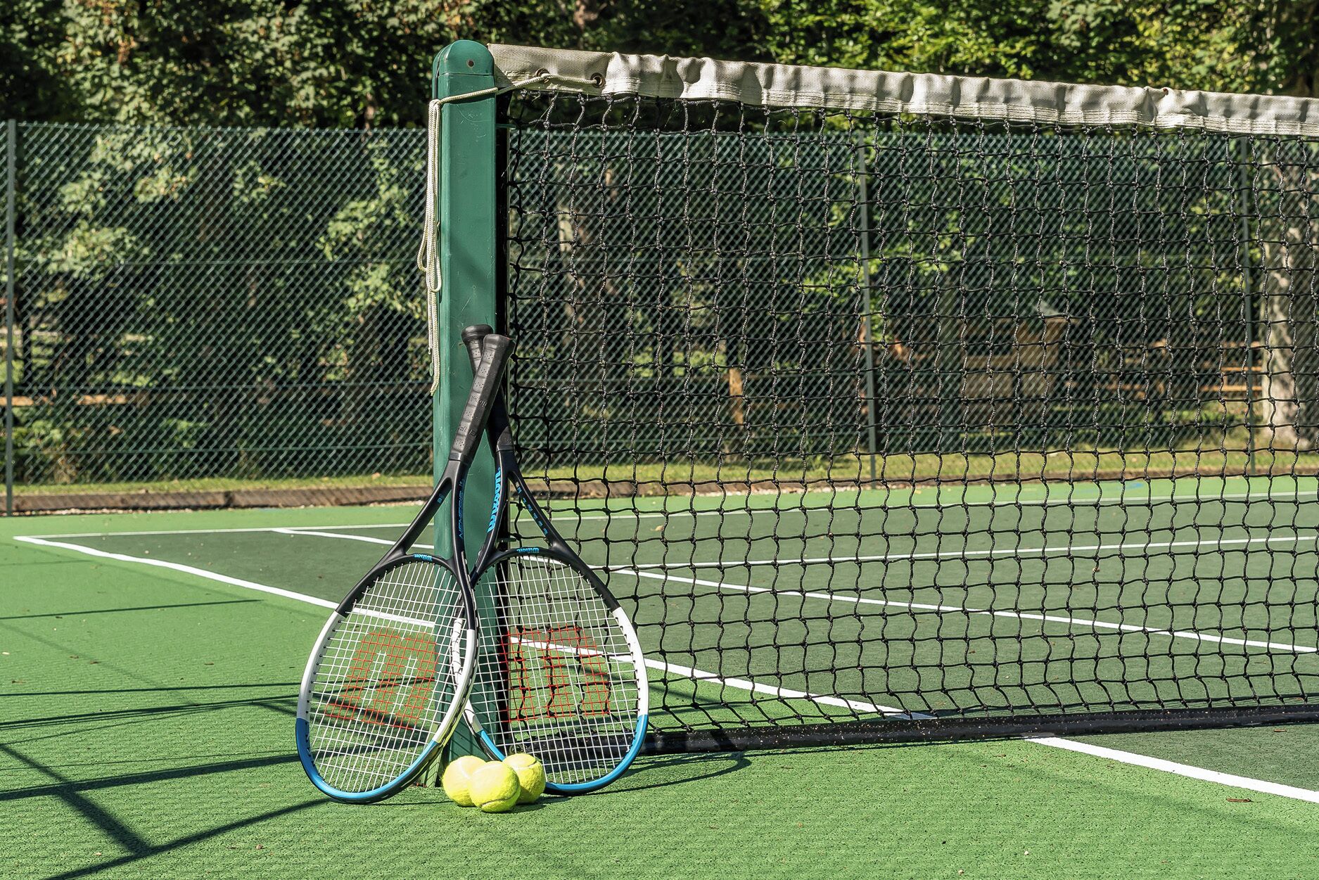 A tennis court with a net, two tennis rackets, and two tennis balls.