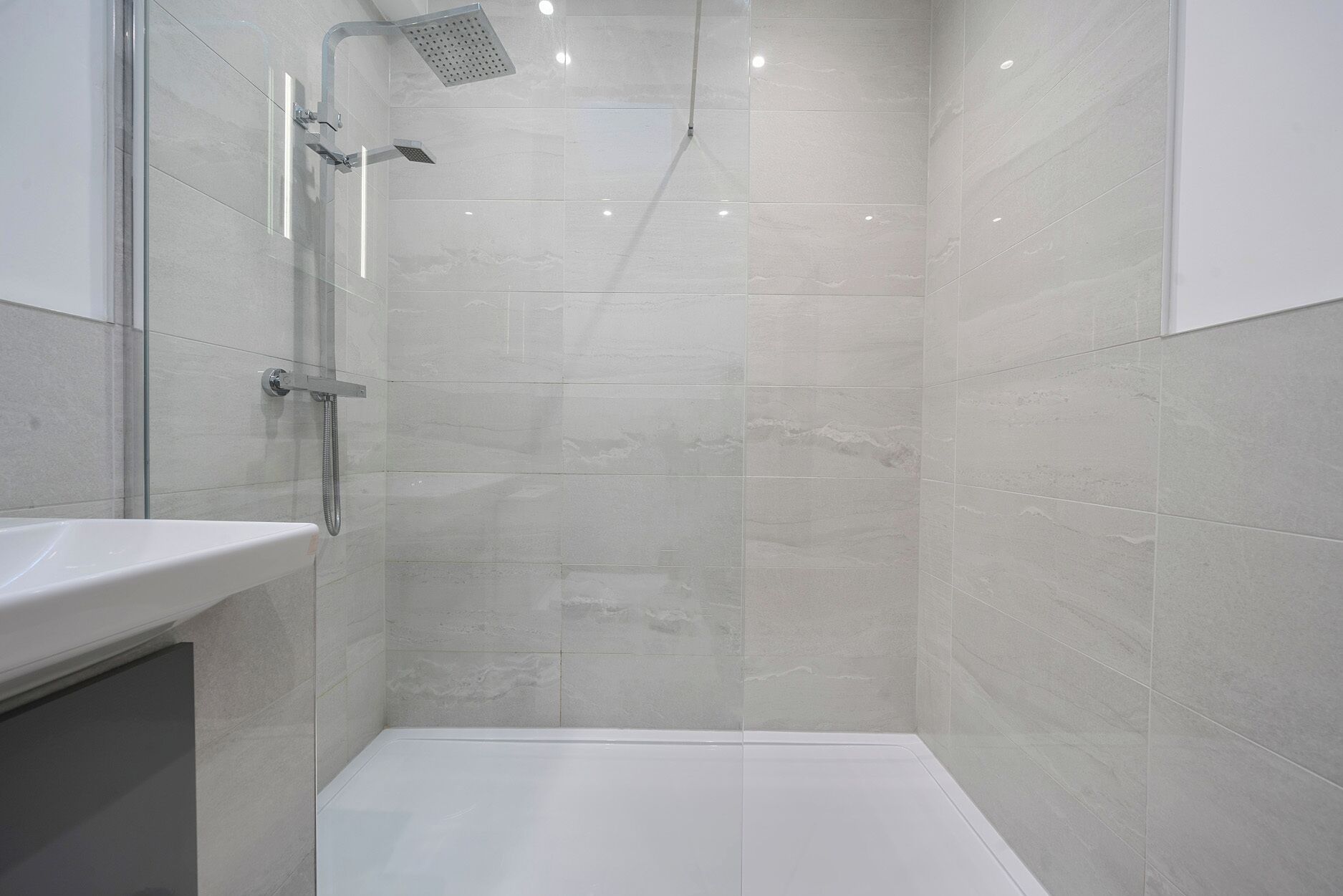 A modern bathroom with a glass shower enclosure, a white sink, and tiled walls.
