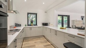 Una cocina moderna con armarios blancos, suelo de madera y ventana con vistas a zonas verdes.