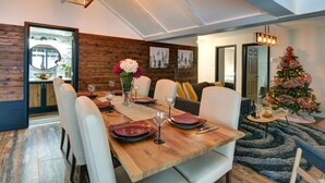 A dining area with a wooden table set for six, white chairs, and a Christmas tree in the background. - Serene Lakefront Cottage Escape (Rivière-Rouge)