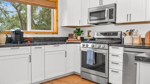 Una cocina moderna con armarios blancos, microondas integrado, estufa y lavavajillas.