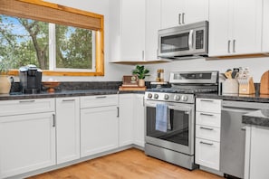 Une cuisine moderne avec des meubles blancs, un four à micro-ondes encastré, une cuisinière et un lave-vaisselle.