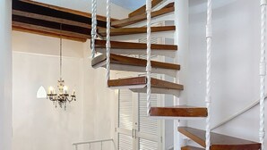 Una escalera en espiral con escalones de madera y barandillas blancas, que conduce a un piso superior.