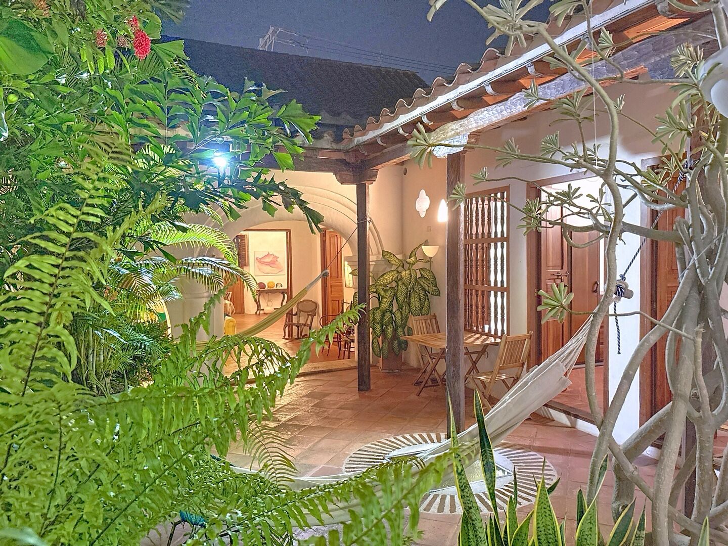 A cozy outdoor patio with a hammock, wooden furniture, and lush greenery.