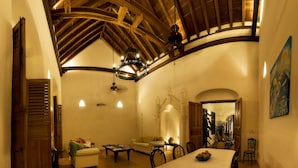 Un área de estar amplia con un techo alto de madera, una mesa de comedor para cuatro y una acogedora disposición de asientos.