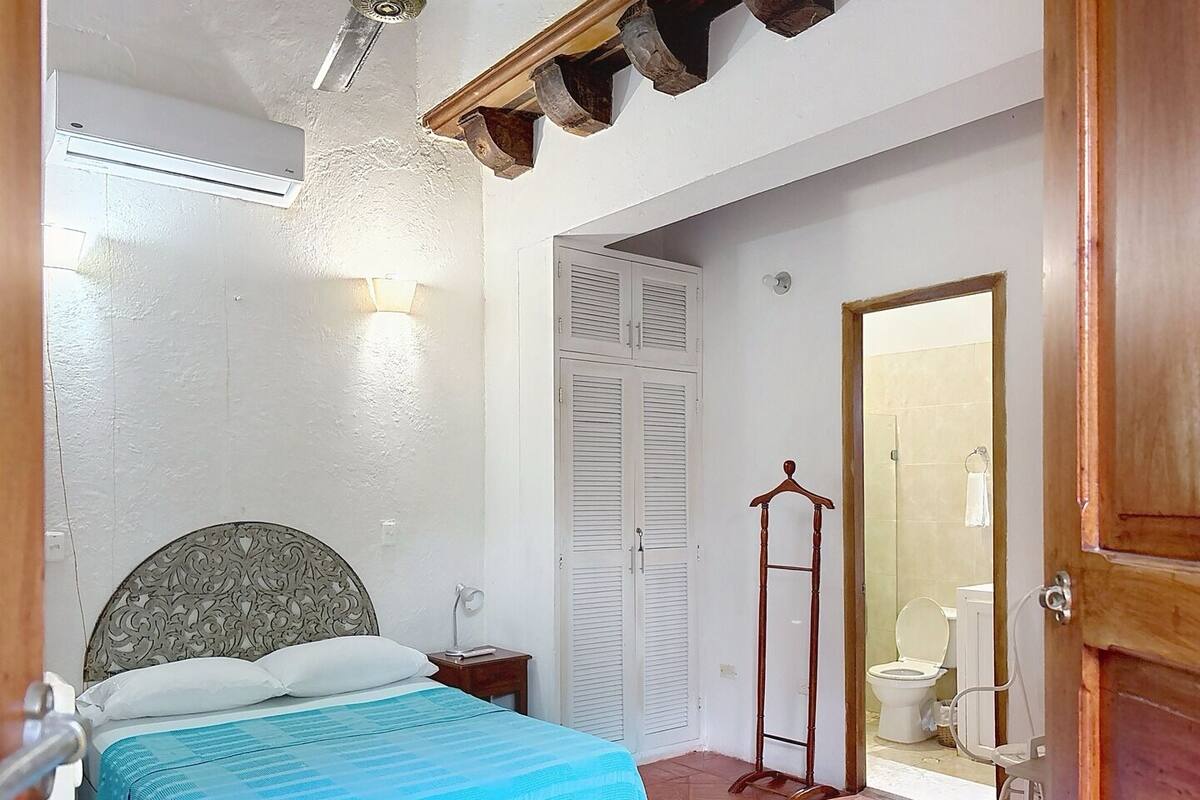 A bedroom with a bed, bedside table, wardrobe, and a bathroom visible through an open door.