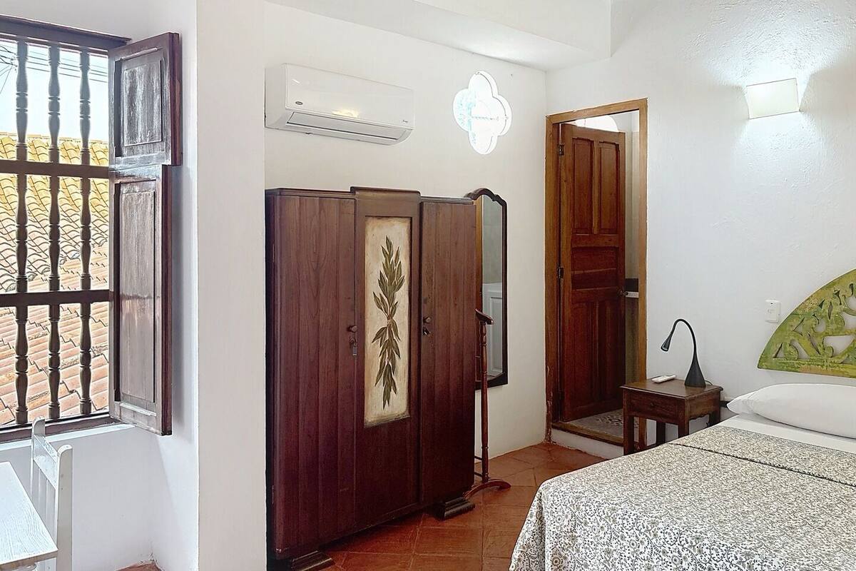 A bedroom with a bed, a wardrobe, a mirror, and an air conditioning unit.