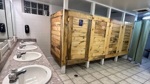 Baño público con tres lavamanos, cabinas de madera y señal de accesibilidad para personas con discapacidad.