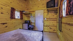 Una cabaña con cama, una kitchenette pequeña, un televisor y una puerta.