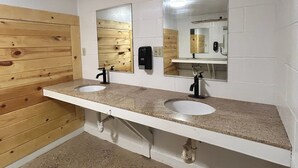A bathroom with two sinks, wooden panel walls, and mirrors. - Sturgis Camping Cabin with Futon and Bunkbed (Sturgis)