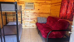 A bunk bed with a red sofa and a patterned pillow, wooden walls, and a window with a curtain. - Sturgis Camping Cabin with Futon and Bunkbed (Sturgis)