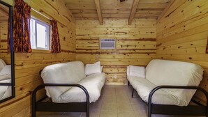 Uma cabana com duas camas de solteiro, uma janela com cortinas, um ventilador de teto e um ar condicionado fixado na parede.