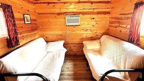 A cabin with two single beds, a wooden interior, and a window with curtains.
